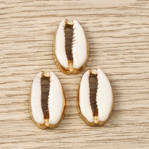 Close-up of three cream cowrie shell pendants with gold plated edges for DIY jewelry