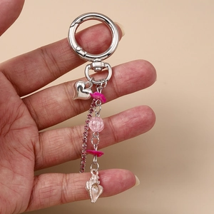 Vue rapprochée du porte-clés argenté avec pendentifs cœur rose et coquillage tenu à la main