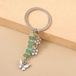 Détail du porte-clés papillon argenté avec pierres vertes et breloques de fleurs