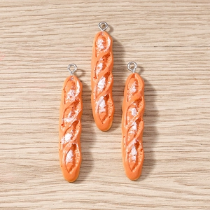Realistic resin baguette bread pendants with metal rings on light wood background
