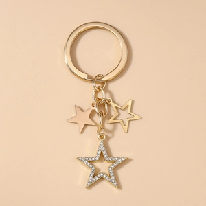Détail de porte-clés étoiles dorées avec strass brillants sur fond beige neutre