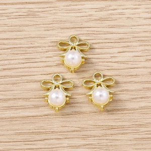 Close-up of golden bow-shaped pearl charms for DIY jewelry making on wood surface