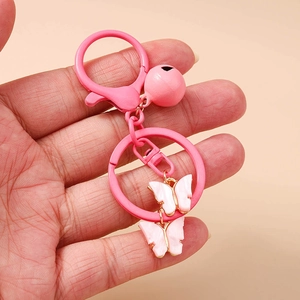 Pink butterfly keychain with bell and resin flower pendant shown in hand for size