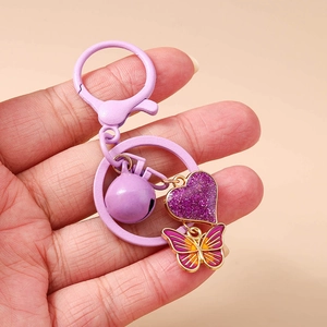 Detailed view of purple bell, glitter heart and enamel butterfly on a metal keychain