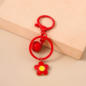Detail of red flower keychain with a small bell and golden-yellow core on matte stone