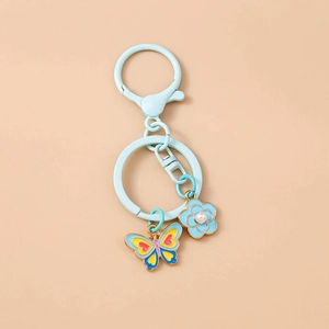 Detailed view of blue metal keychain with enamel butterfly and pearl-centered flower pendant