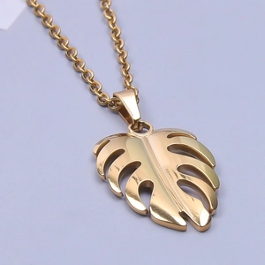 Macro detail of a 18k gold plated monstera leaf pendant necklace on a blue background