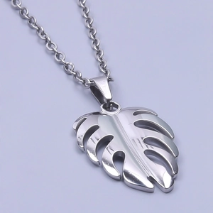 Macro shot of polished silver Monstera leaf pendant on a thin cross chain necklace