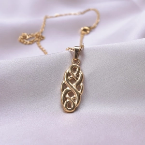 Detailed close-up of golden Celtic knot necklace pendant on elegant purple silk fabric background