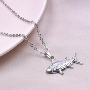 Dettaglio della collana con ciondolo a forma di pesce in acciaio inox su un piatto ceramico