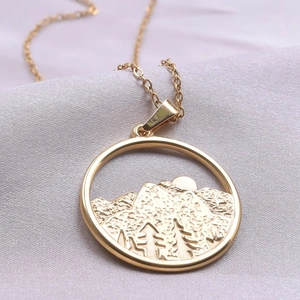 Gros plan d'un pendentif montagne circulaire plaqué or sur un satin gris soyeux