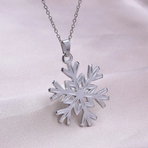 Close-up of a silver-toned snowflake pendant necklace on a soft silk fabric background