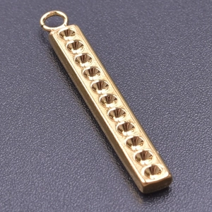 Macro detail of golden rectangular pendant with ten conical grooves and top circular loop