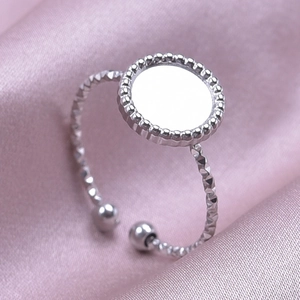Primer plano de anillo plateado con bisel redondo milgrain sobre fondo de raso rosa