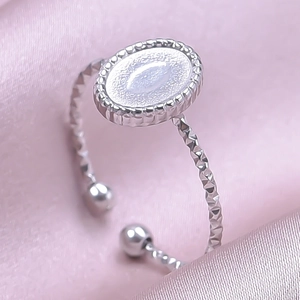 Detalle de anillo ovalado plateado con incrustación blanca y banda de corte diamante