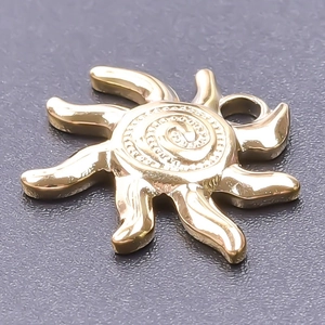 Macro shot of gold sun pendant with radiant rays and spiral texture on grey background
