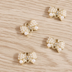 Vue détaillée de quatre breloques nœuds dorés avec perles et strass pour bijoux DIY
