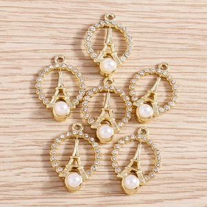 Close-up of golden Eiffel Tower charms with rhinestones and white pearls on wood surface