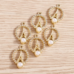 Detailed view of gold Eiffel Tower charms with rhinestones and white pearls on wood