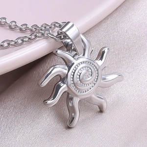 Macro detail of sun pendant necklace in silver finish on pink satin background
