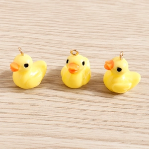 Three yellow resin duck pendants with golden metal loops on a wood surface
