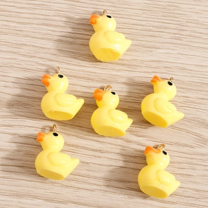 DIY yellow resin duck charms with golden metal loops on light wood background