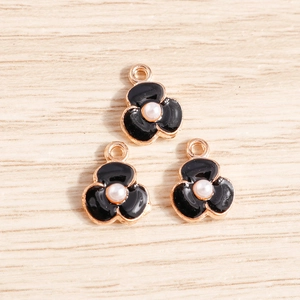 Détail de trois breloques fleurs en émail noir avec perles et placage en or rose pour DIY