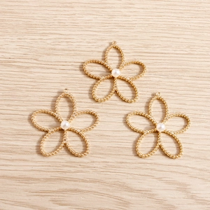 Detail view of 3 gold hollow plum blossom pendants with white pearls on wood surface