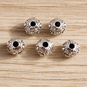 Five vintage silver zinc alloy barrel beads with intricate relief patterns on wood background