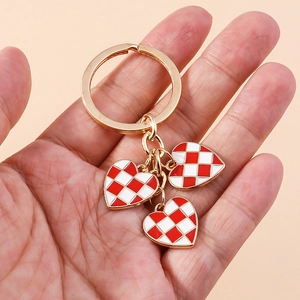 Fashionable gold checkered heart keychain with three red and white enamel charms on hand