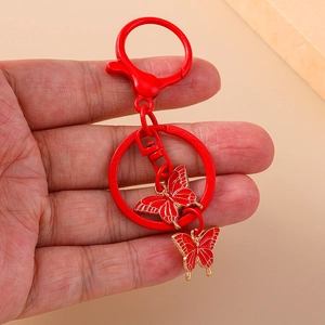 Vibrant red butterfly keychain with bell and lobster clasp, handheld for size reference