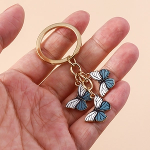Détail macro de trois breloques papillon dorées avec rayures bleues et blanches sur porte-clés