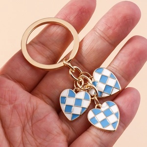 Close-up of blue and white checkered heart charms on a golden metal keychain held in hand