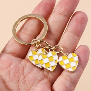 Detail of checkered heart keychains with gold plating held against a soft pink background