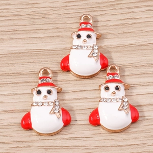 Detail of three snowman charms with red and white enamel and rhinestones on wood background