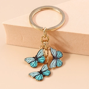 Vue détaillée de trois pendentifs papillons bleus avec anneaux dorés sur fond doux