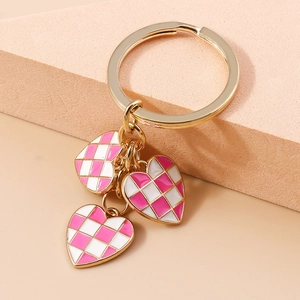 Detail of golden heart-shaped keychain with three pink checkered enamel heart charms