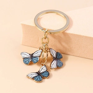 Détail d'un porte-clés papillon doré avec des breloques en émail bleu et blanc