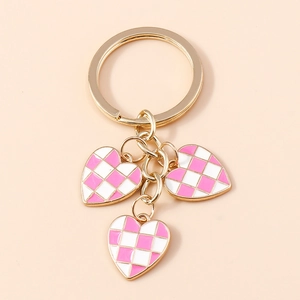 Macro detail of checkered heart charms and golden key ring with pink enamel finish