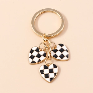 Detailed close-up of golden checkered heart keychain pendants on a light beige background