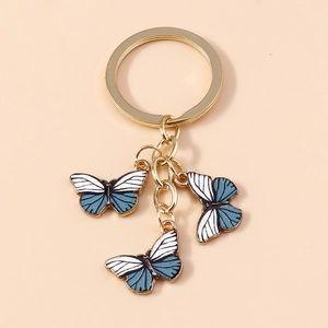 Détail d'un porte-clés papillon doré avec breloques en émail bleu et blanc poli