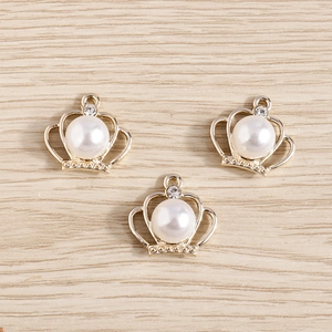 Three elegant crown pendant charms with pearls and rhinestones on wood surface