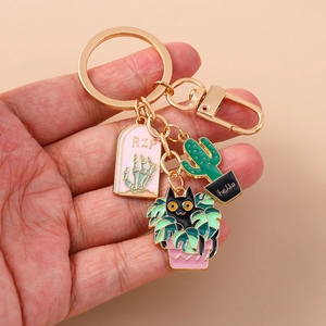 Detail of hand holding a gold keychain with pink RIP tombstone and cat cactus charms