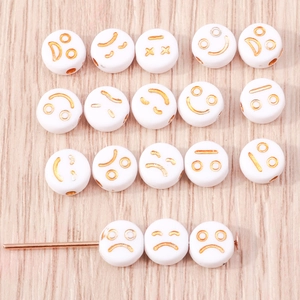 Dettaglio di perline in acrilico bianco con motivi emoji dorati per gioielli fai-da-te
