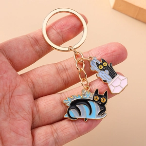 Macro view of cartoon black cat keychain with gold-plated edges and blue leaf enamel charms