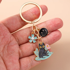 Close-up of black cat and blue flower enamel pendants on a gold keychain ring