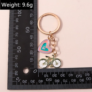 Détail de breloques cœur et vélo en émail coloré sur un porte-clés en or rose avec règle