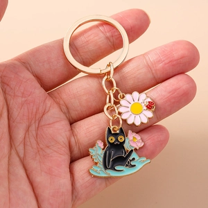 Detailed close-up of a golden alloy black cat keychain with pink daisy and ladybug charm