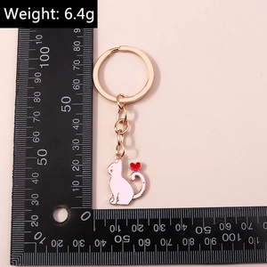 Porte-clés chat en émail rose avec cœur rouge et finition dorée présenté avec une règle