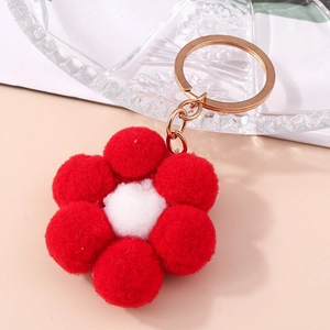 Plush red flower keychain with white center and gold metal ring on pink background